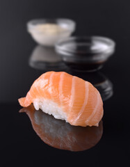 Salmon nigiri reflecting on dark surface with soy sauce and wasabi