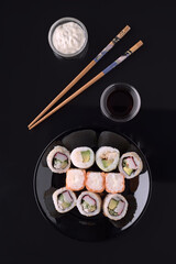 Sushi set with soy sauce, mayonnaise and chopsticks on black background