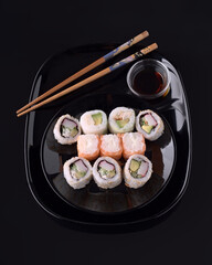 Sushi rolls with soy sauce and chopsticks on black plate