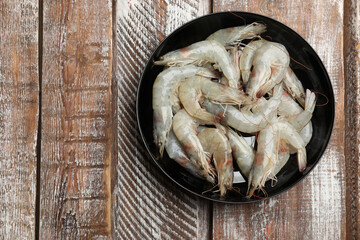 Fresh raw shrimps in bowl on wooden table, top view. Space for text