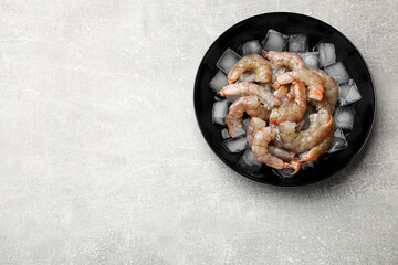 Fresh raw shrimps with ice cubes in bowl on grey table, top view. Space for text