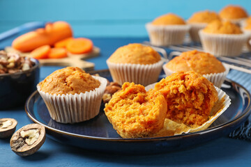 Tasty carrot muffins and walnuts on blue wooden table, closeup