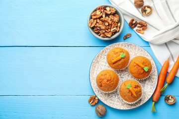 Tasty carrot muffins, walnuts and fresh vegetables on light blue wooden table, flat lay. Space for text