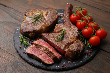 Pieces of delicious beef meat, spices and tomatoes on wooden table, closeup