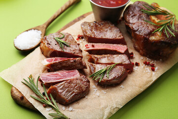 Pieces of delicious beef meat, spices and sauce on green background, closeup