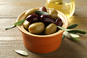 Tasty olives and leaves in bowl on wooden table, closeup