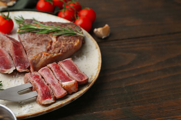 Pieces of delicious beef meat, spices and tomatoes on wooden table, closeup. Space for text