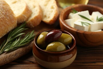 Delicious marinated olives, bread and feta cheese served on wooden table, closeup