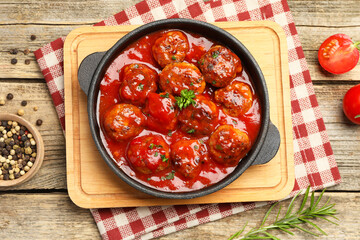 Delicious meatballs with tomato sauce in baking dish and spices on wooden table, flat lay