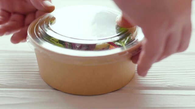 Closeup of man paking up a fresh healthy salad to a zero waste container to go. Food delivery, healthy food concept.