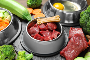 Pet food. Fresh beef in feeding bowl and chew bone among products on table, closeup