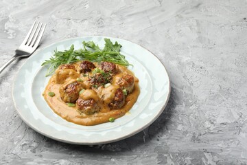 Delicious meatballs with gravy cream sauce, herbs and arugula served on grey table. Space for text