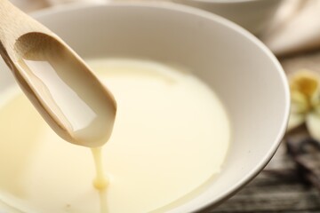 Taking tasty vanilla condensed milk with spoon from bowl on table, closeup