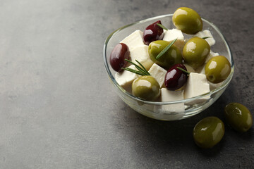 Tasty olives with feta cheese in glass bowl on grey textured table, closeup. Space for text