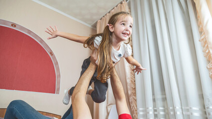 Obraz premium Cheerful small girl daughter and her handsome young dad spending time together at home.