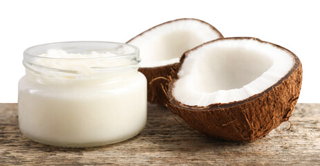 Organic coconut cooking oil in glass jar and halves of fresh fruit on wooden table against white background
