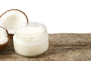 Organic coconut cooking oil in glass jar and halves of fresh fruit on wooden table against white background