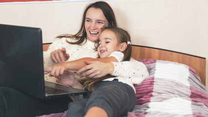 Young woman using laptop computer with her daughter while lying on bed in bedroom