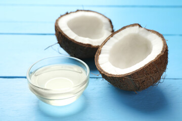 Organic coconut cooking oil in glass bowl and halves of fresh fruit on light blue wooden table, closeup
