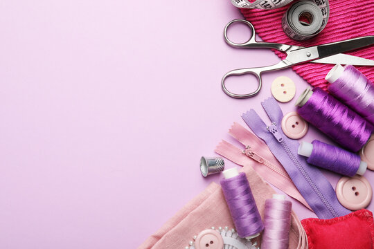 Different sewing supplies on lilac background, flat lay. Space for text