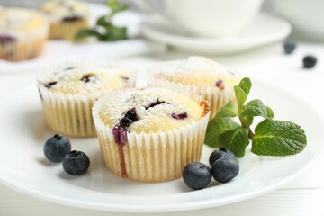 Delicious muffins with blueberries, powdered sugar and mint on white wooden table, closeup