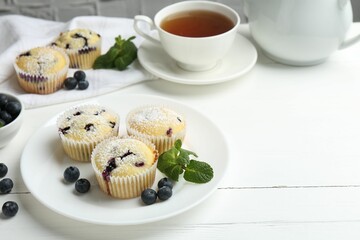 Delicious muffins with blueberries, powdered sugar and mint on white wooden table. Space for text