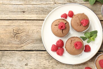 Delicious muffins with raspberries and mint on wooden table, flat lay. Space for text