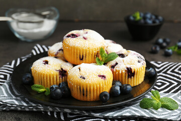 Delicious muffins with blueberries, powdered sugar and mint on dark table, closeup