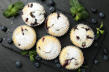 Delicious muffins with blueberries, powdered sugar and mint on dark textured table, flat lay