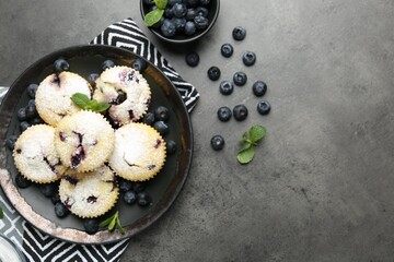 Delicious muffins with blueberries, powdered sugar and mint on dark textured table, flat lay. Space for text