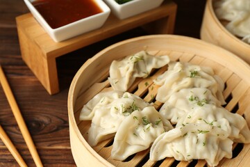 Tasty boiled gyoza (dumplings) in bamboo steamers, sauce and chopsticks on wooden table, closeup