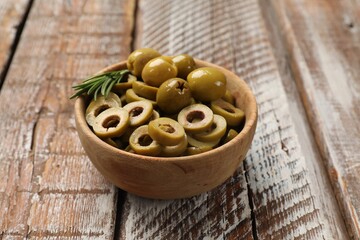 Delicious marinated olive rings, rosemary and whole ones in bowl on wooden table, closeup