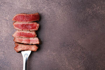 Delicious sliced beef tenderloin with different degrees of doneness on brown textured table, top view. Space for text