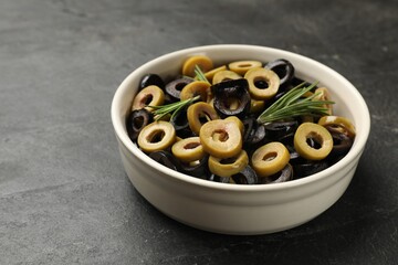 Different delicious marinated olive rings and rosemary in bowl on dark textured table, closeup. Space for text