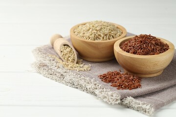 Different types of brown rice in bowls and scoop on white wooden table, closeup. Space for text
