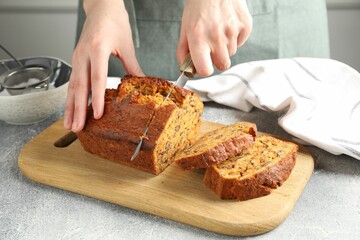 Woman cutting homemade carrot cake at grey table, closeup