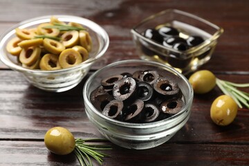 Different delicious marinated olive rings, whole ones and rosemary on wooden table, closeup