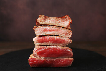 Delicious sliced beef tenderloin with different degrees of doneness on table against brown background, closeup