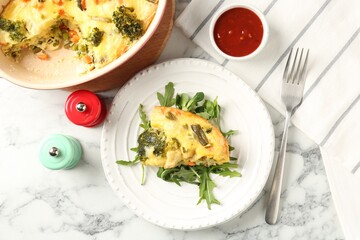 Tasty vegetable casserole, arugula, shakers, sauce and fork on white marble table, flat lay