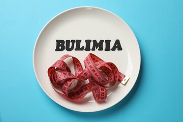 Plate with word Bulimia and measuring tape on light blue background, top view