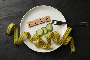 Bulimia. Plate with word Help, pieces of cucumber, measuring tape and fork on dark textured...