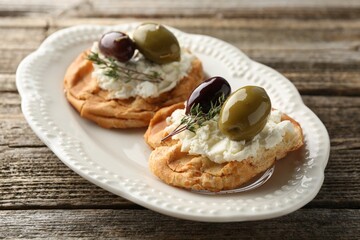 Delicious sandwiches with marinated olives, cream cheese and thyme on wooden table, closeup
