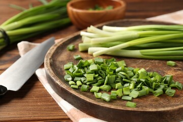Fresh green onions and knife on wooden table, closeup
