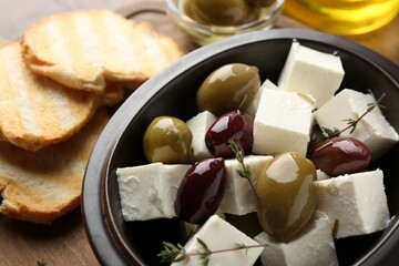 Marinated olives with feta cheese, rosemary and bread pieces on table, closeup