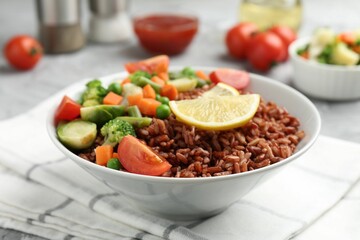 Delicious brown rice with vegetables and lemon slices served on grey table, closeup