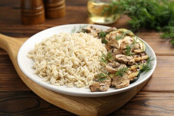 Delicious brown rice with mushrooms and dill served on wooden table, closeup
