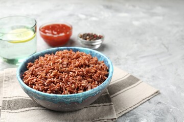 Delicious brown rice served on grey textured table, closeup. Space for text