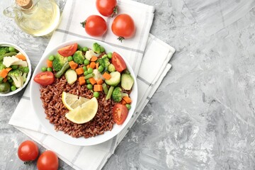 Delicious brown rice with vegetables and lemon slices served on grey textured table, flat lay. Space for text