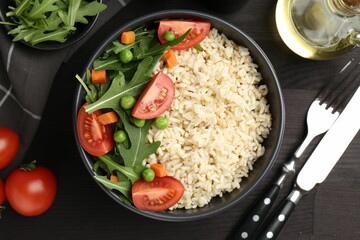 Delicious brown rice with vegetables served on black wooden table, flat lay