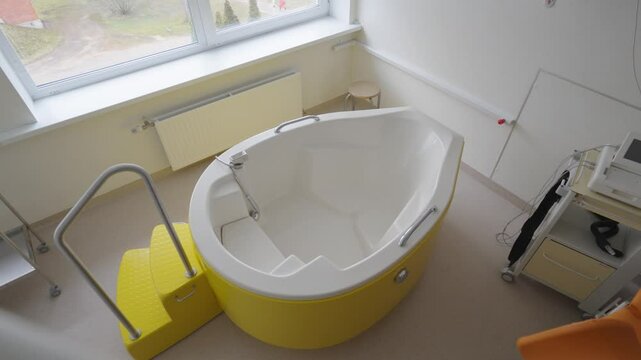 Modern birthing room with a yellow water birth tub, medical equipment, and clean surroundings designed for comfort and safe labor.